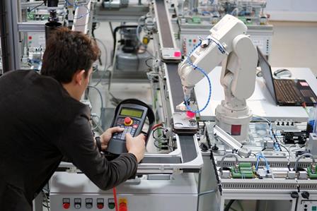 Engineer holding a teach panel to control a robotic arm Master of Engineering (Industrial Automation) degree