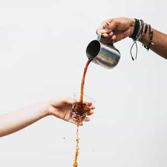 Man holding jug pours coffee into glass cup