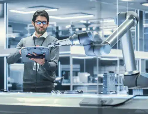 Postgraduate engineering student programming an industrial robotic arm in an advanced automation research laboratory.